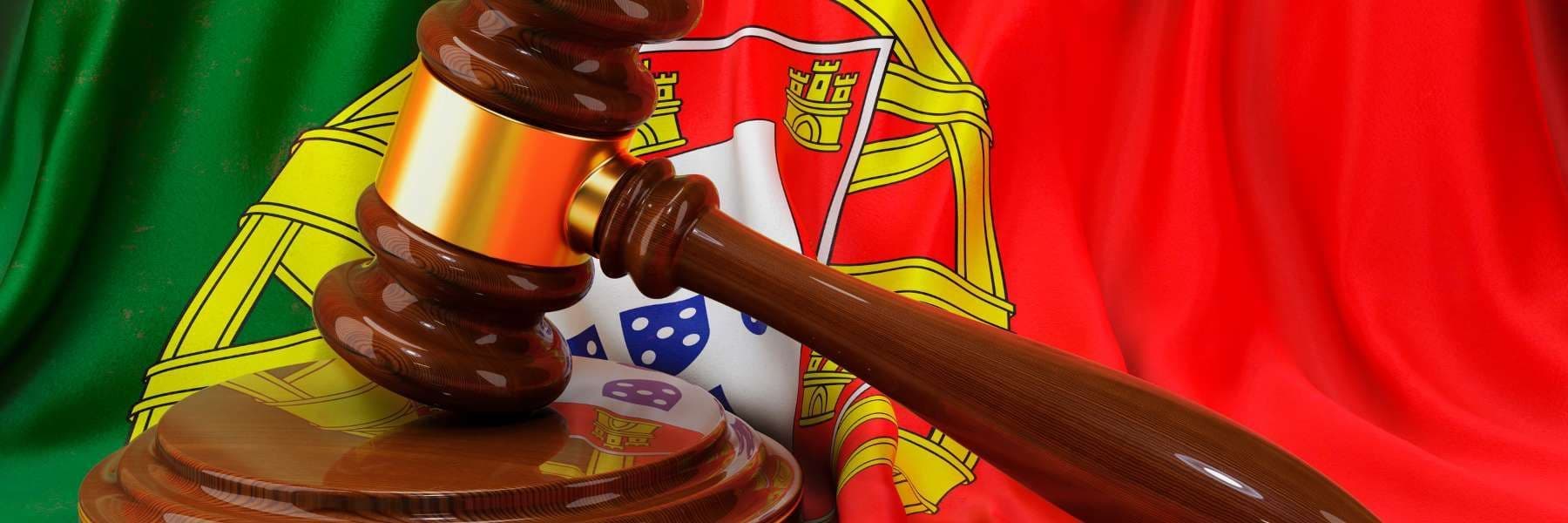 A wooden judge’s gavel resting on its sound block in front of a draped Portuguese flag.