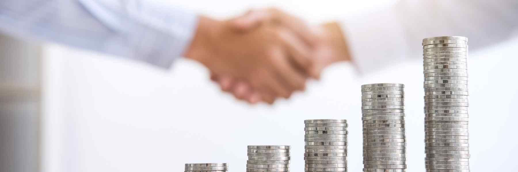 Shaking hands with a pile of coins in the background